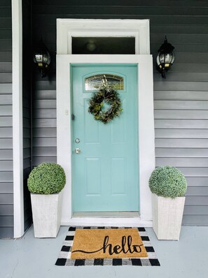A teal front door with a wreath, two potted plants, and a black and white checkered doormat with "hello" written on it.