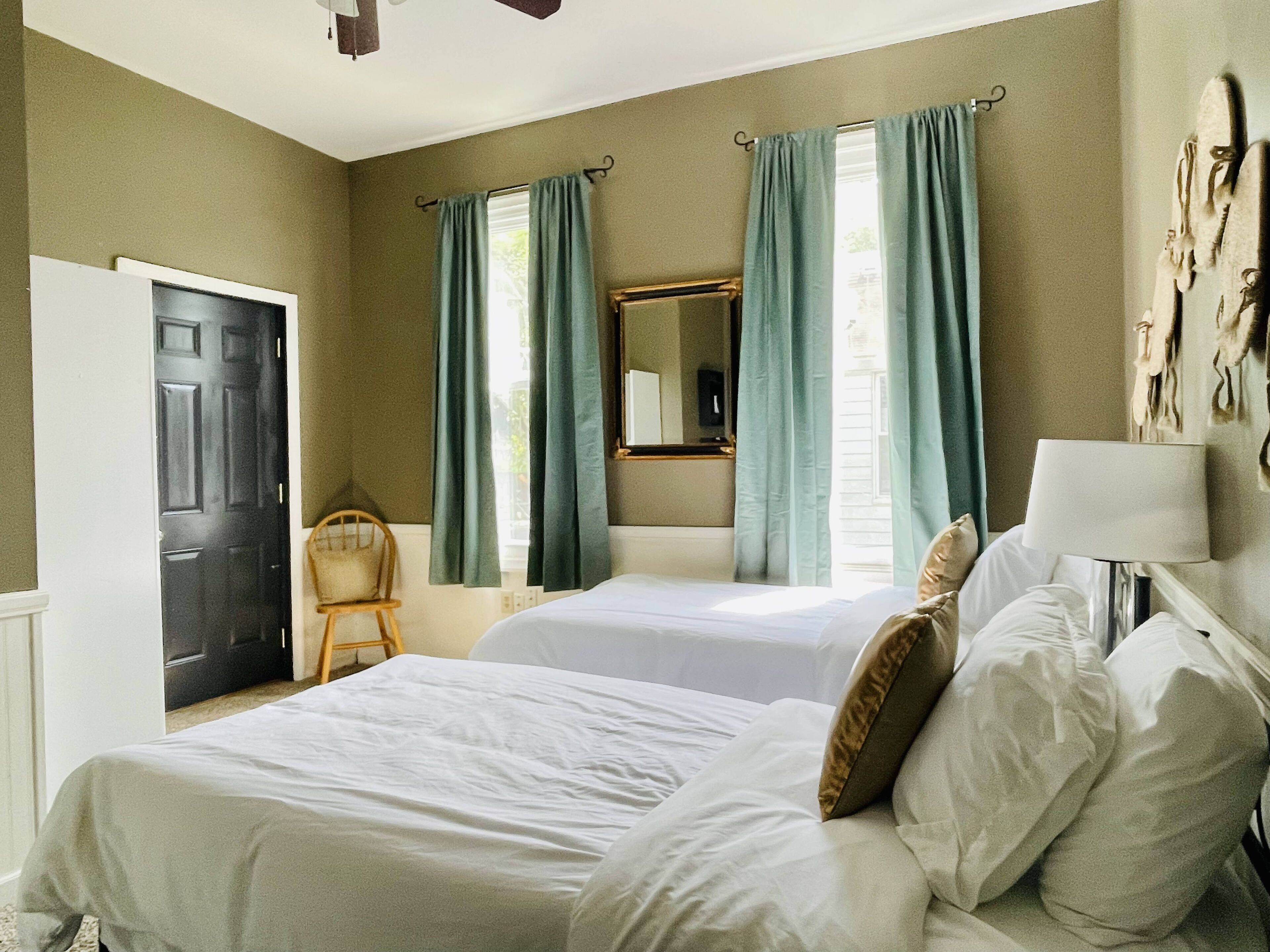 Une chambre d’hôtel avec deux lits, une chaise, un bureau, un miroir et des rideaux.