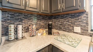 A kitchen with grey cabinets, a stone backsplash, a Keurig coffee maker, and a coffee station with mugs and a tray of coffee pods. - Discover Durham, just a quick 11-minutes from Duke University (Durham)