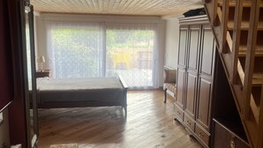 A bedroom with a bed, wooden floor, wardrobe, and a sliding glass door leading to an outdoor area.