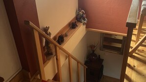 A wooden staircase with a handrail, a small table with a vase and a clock, and a window with a picture frame.
