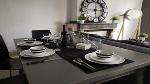 Un tavolo da pranzo apparecchiato con piatti, bicchieri e posate, con una sveglia e oggetti decorativi sullo sfondo.