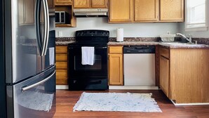 Cucina con mobili in legno, frigorifero nero, piano cottura, lavastoviglie e forno a microonde.
