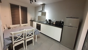 Una cocina compacta con una mesa de comedor y sillas, horno empotrado, cafetera y refrigerador.