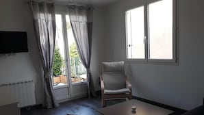 Una sala de estar moderna con un sofá, una mesa de centro, un reposapiés acolchado, una silla y un televisor en la pared.