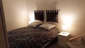 Una cama bien hecha con una colcha estampada, dos almohadas y una lámpara de noche sobre una mesita.