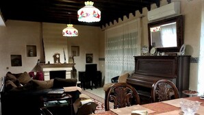 Ein gemütliches Wohnzimmer mit einer Couch, einem Klavier, einem Esstisch mit Platzdeckchen und einer Pendelleuchte.