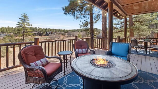 A covered outdoor deck with wicker chairs, a round table with a fire pit, and a view of a forested landscape. - 5 🌟 Luxury Torreon  (Show Low)