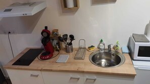 A kitchen with a stainless steel sink, a red coffee maker, a microwave, and various kitchen utensils.