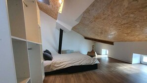 Un dormitorio amplio en el ático con suelo de madera, una cama y estanterías empotradas.