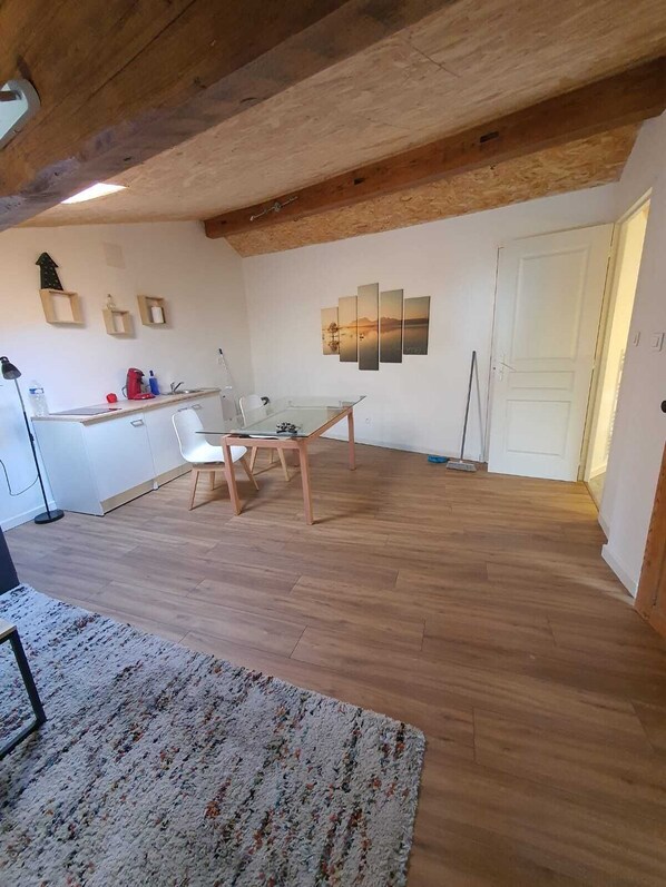 A spacious kitchen with wooden flooring, a dining area with a glass table, and a white door.