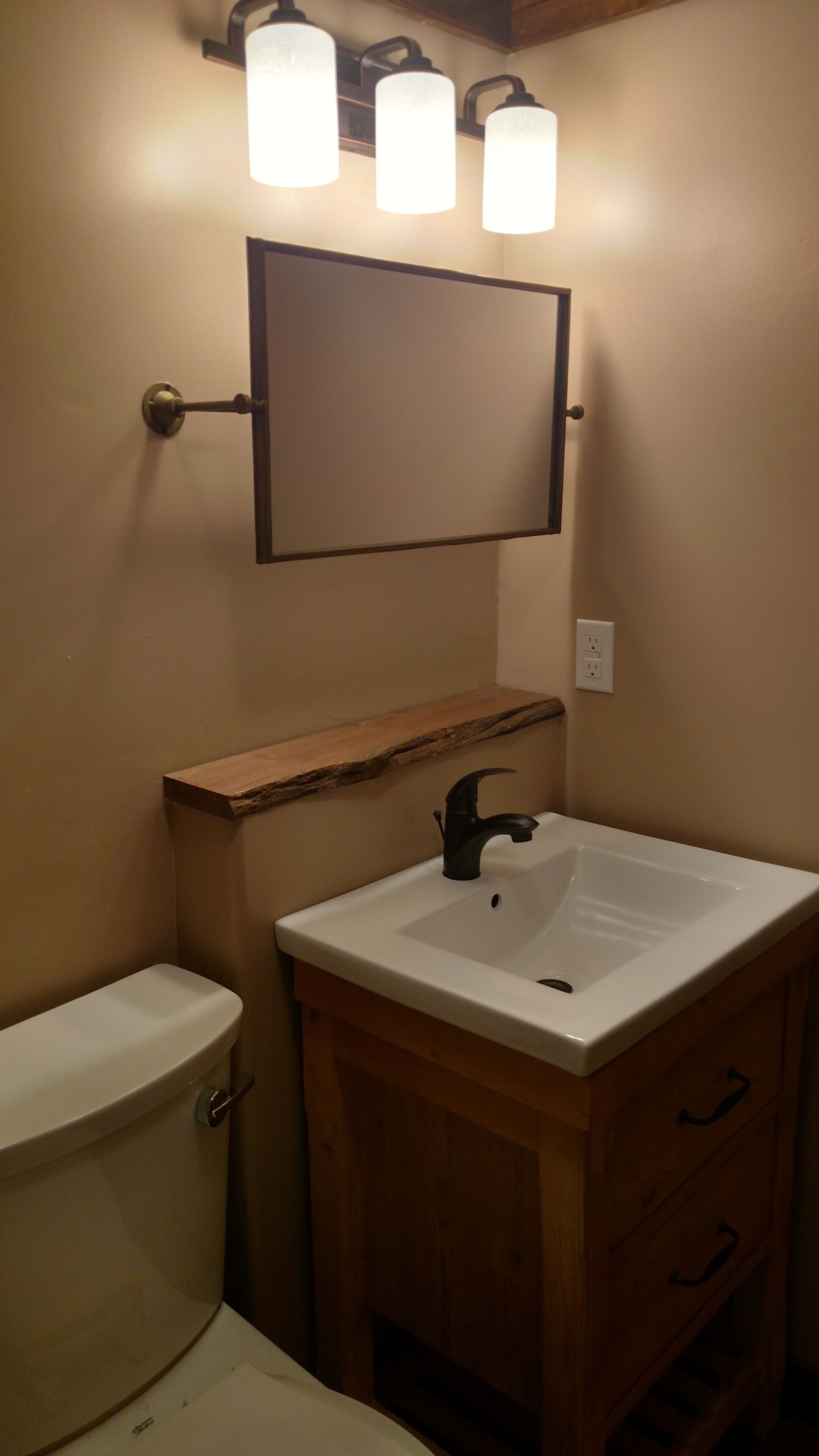 Un baño con inodoro, lavabo y espejo. Hay tres luces sobre el espejo.