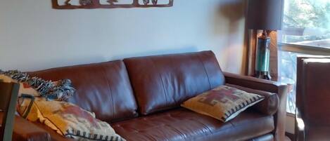 A living room with a brown leather sofa, a patterned rug, and a wall art piece.