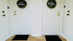 Två vita dörrar med svarta dörrmattor och kransar med texten ”River City Retreat” och ”Heavensville Haven”.