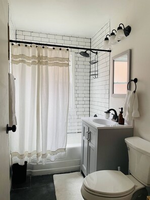 Een badkamer met een witte badkuip, een witte wastafel met een zeepdispenser, een toilet en een douche met gordijn.