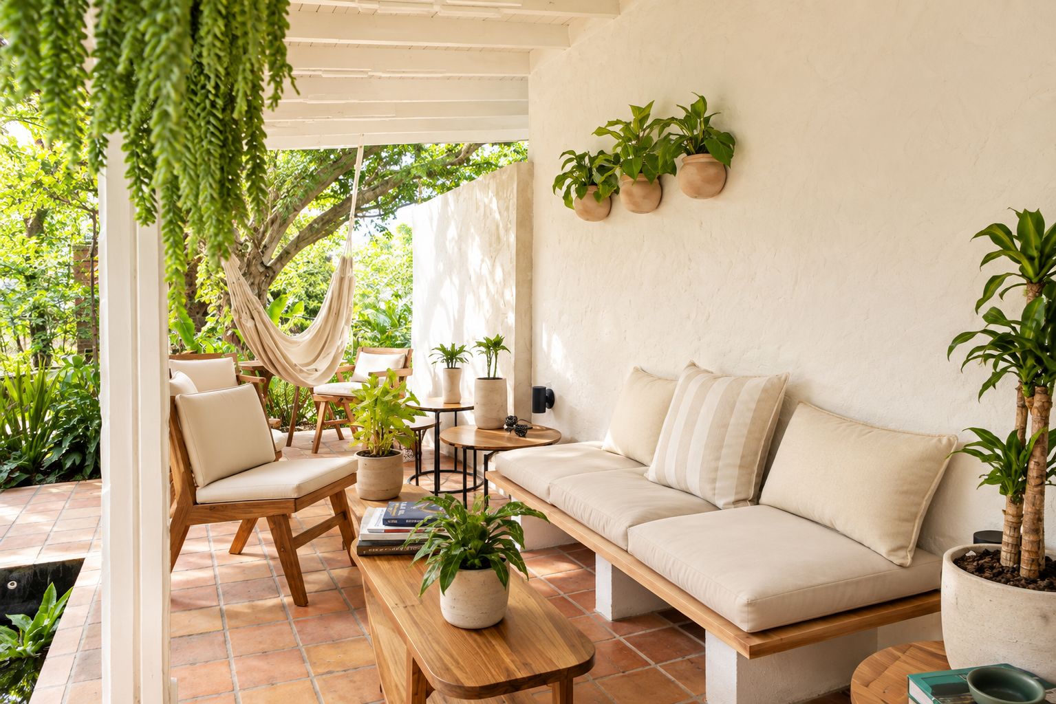 Un patio acogedor con sofá, sillas, una hamaca y plantas en macetas.