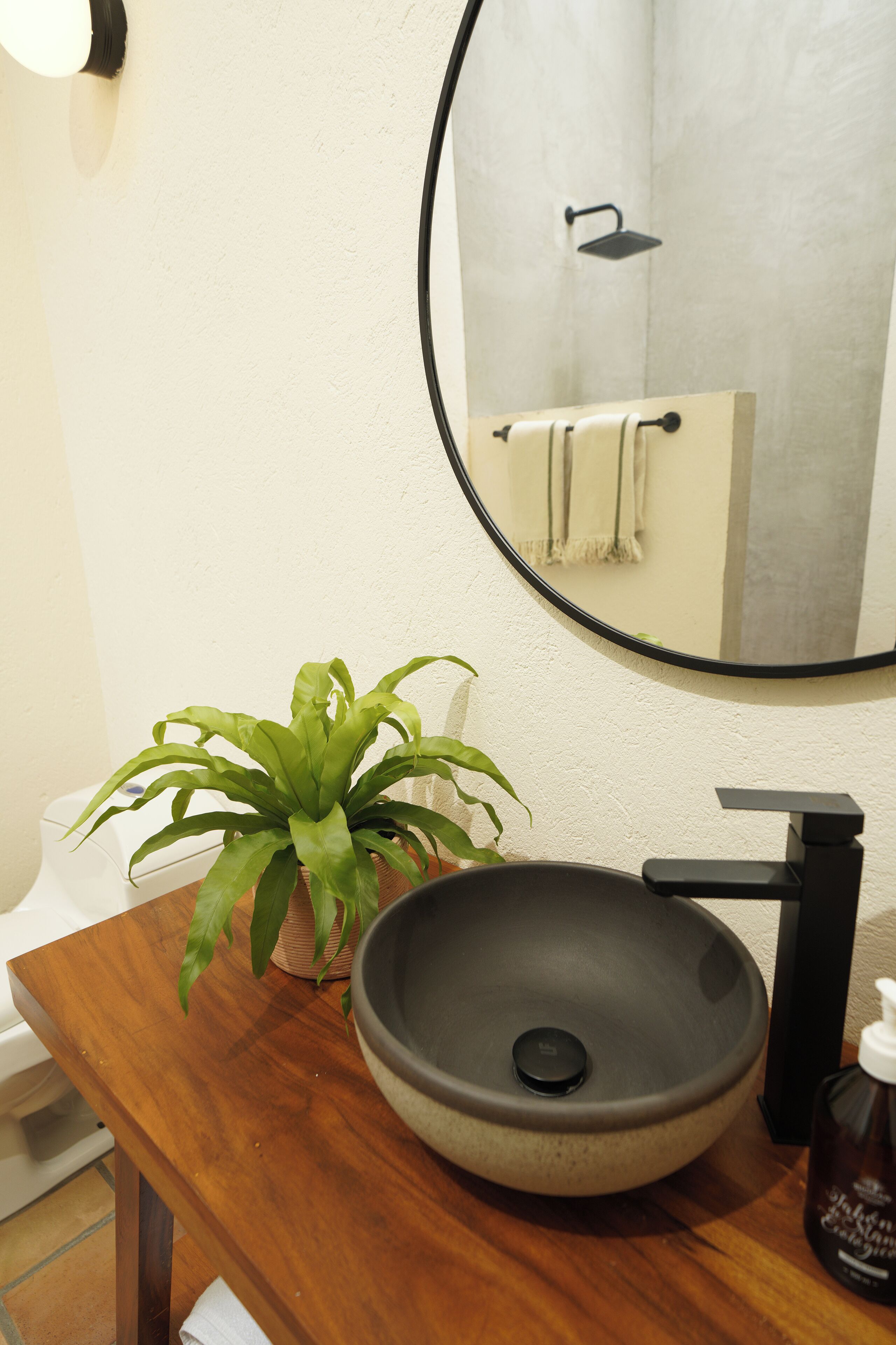 A bathroom with a wooden vanity, a round vessel sink, a potted plant, a mirror, and a towel rack.