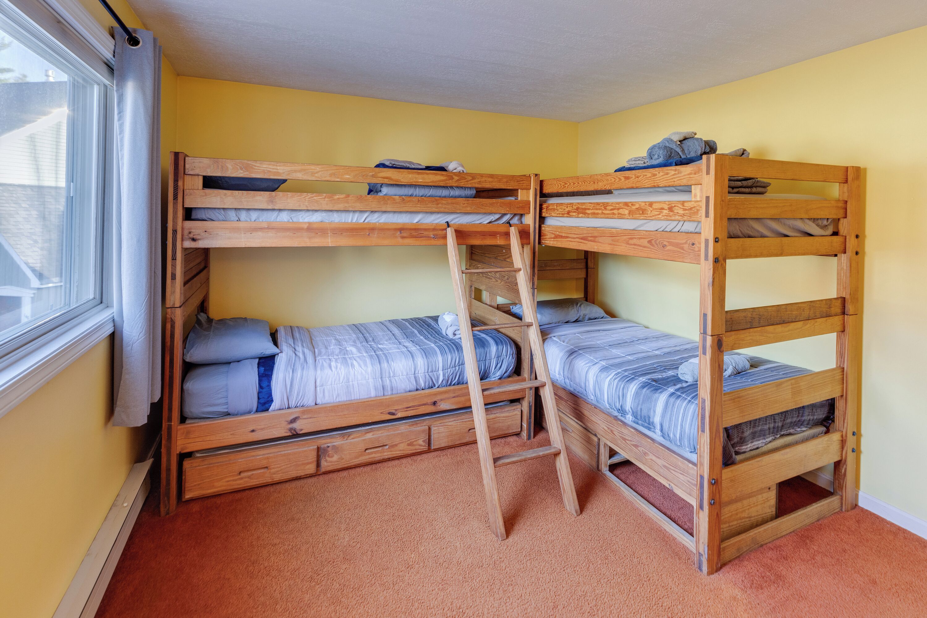 Habitación con literas, una ventana, escalera de madera y piso alfombrado.