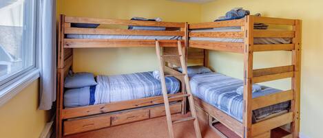 Habitación con literas, una ventana, escalera de madera y piso alfombrado.