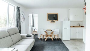 Una sala moderna con un sofá, una mesa de comedor con sillas, un televisor y una zona de cocina con armarios y un refrigerador.