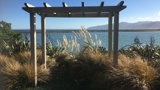 Una pérgola de madera con vistas a un cuerpo de agua tranquilo y montañas distantes.