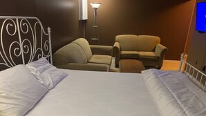 Een hotelkamer met een bed, twee fauteuils, een bank en een vloerlamp.