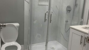 Een moderne badkamer met een glazen douchecabine, toilet en kast.
