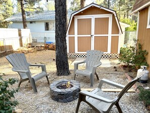Un jardin avec un foyer en pierre, deux fauteuils Adirondack et un abri en bois.