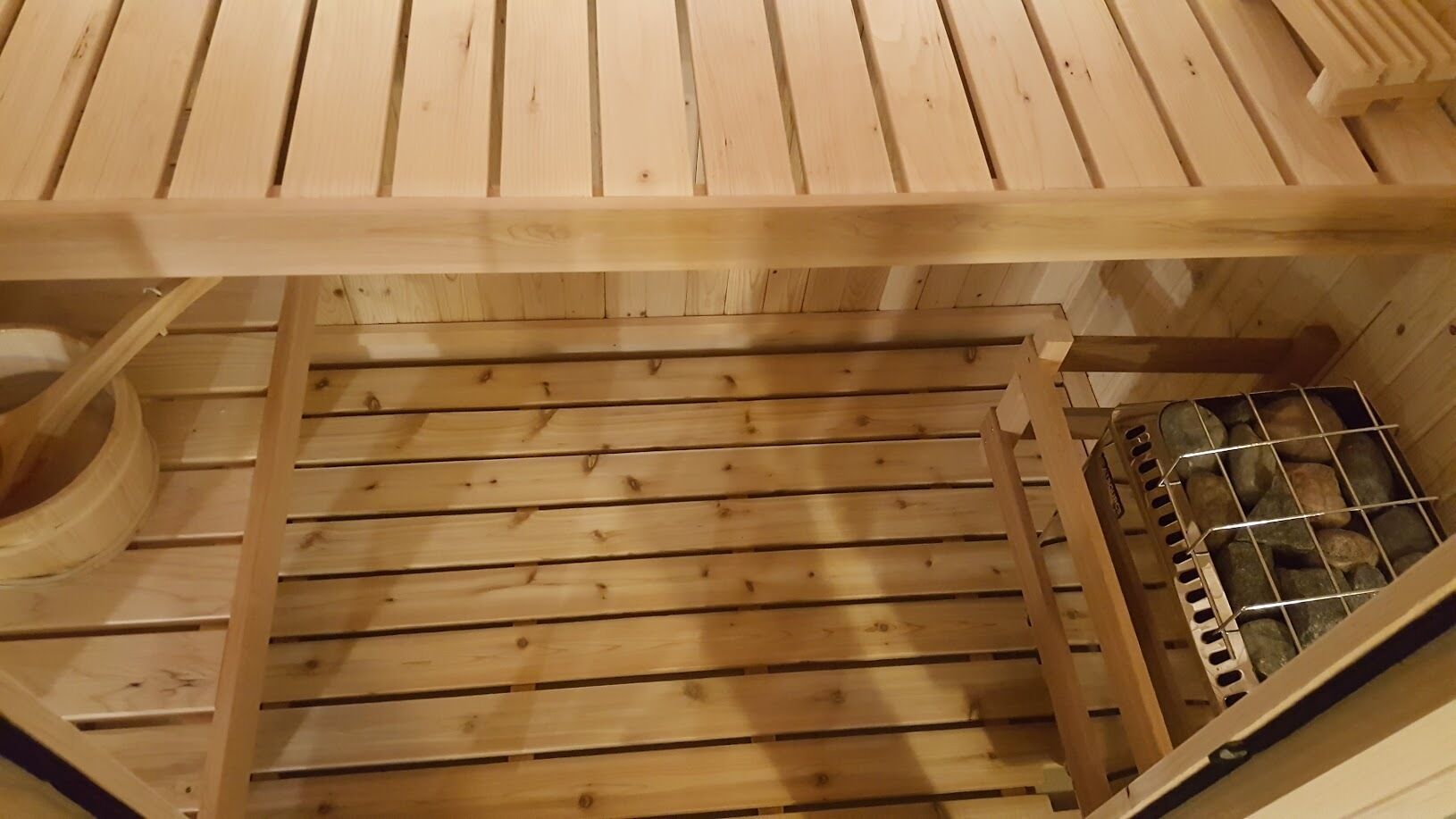 A wooden sauna with a slatted floor and a metal grate filled with stones.
