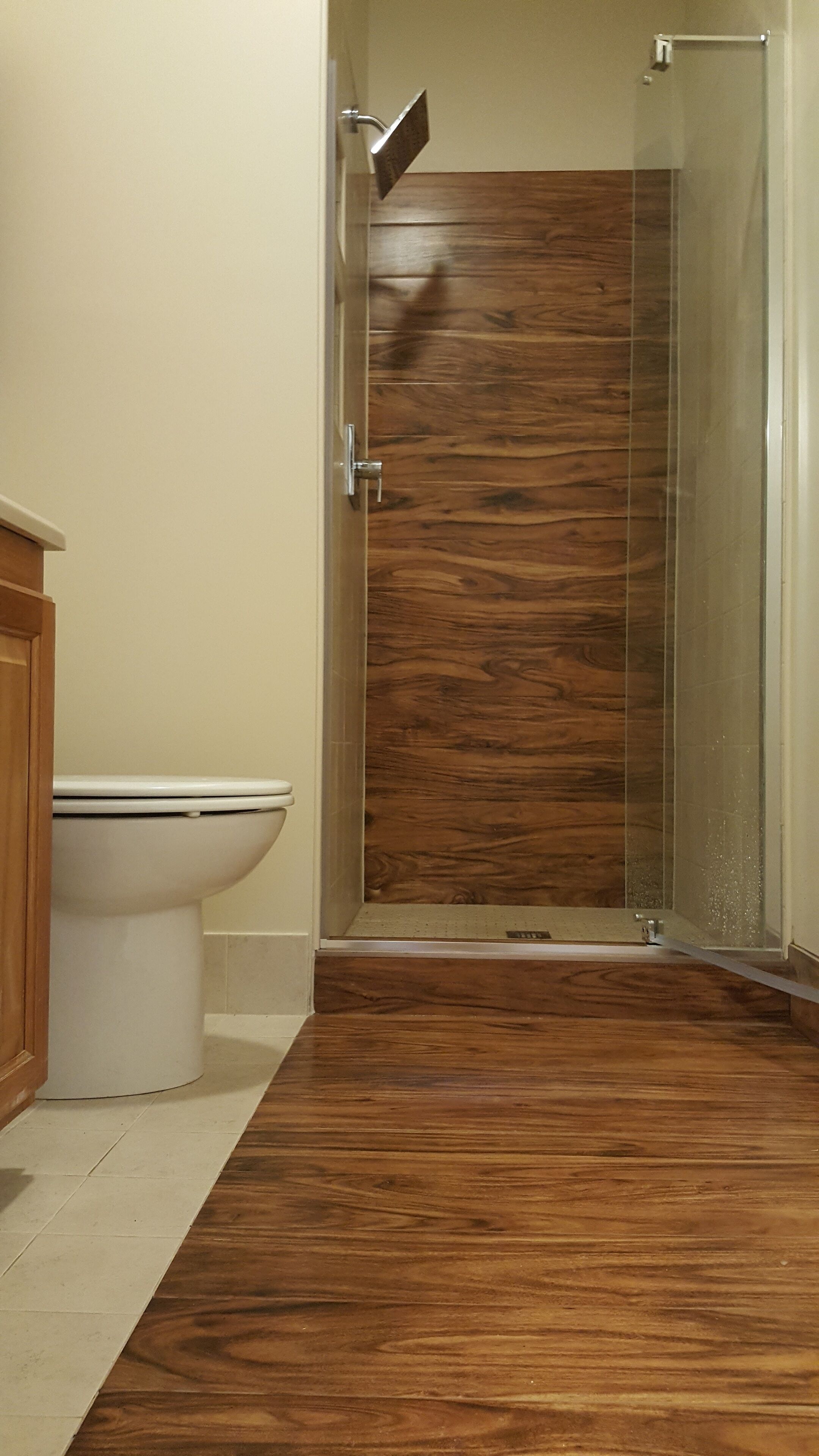 A bathroom with a toilet, a shower with a glass door, and wooden flooring.