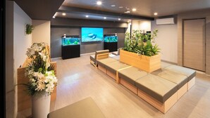 A modern waiting area with a sofa, aquarium, and a large plant. - WELLSTAY Shinsekai Wakyo (Osaka)