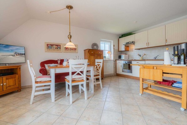Uma cozinha espaçosa com armários brancos, uma área de refeições com mesa e cadeiras de madeira, e uma grande janela que oferece luz natural.