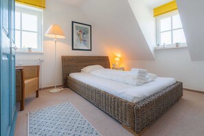 Quarto com cama de vime, luminária de cabeceira, quadro emoldurado e janela com vista.