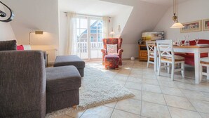 A cozy living room with a sofa, ottoman, and a dining area with a table and chairs. - Apartment 4 Müller (ID 425) (Sankt Peter-Ording)