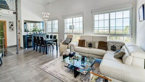 Amplia sala de estar con diseño moderno, que incluye una mesa de centro de vidrio, un sofá color beige y un comedor con mesa y sillas de madera oscura.