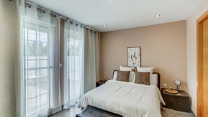 Un dormitorio con cama, banca, mesita de noche, espejo y ventana con cortinas.