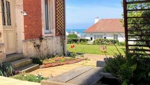 A wooden deck with a planter box, a red brick building, and a grassy yard with a bench. - Les Alcyons - Villa Belle Époque sea view, garden & folly, 13 pers. (Fécamp)
