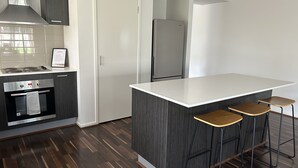Une cuisine moderne dotée d’un îlot central, de tabourets de bar, d’un four encastré et d’un réfrigérateur.