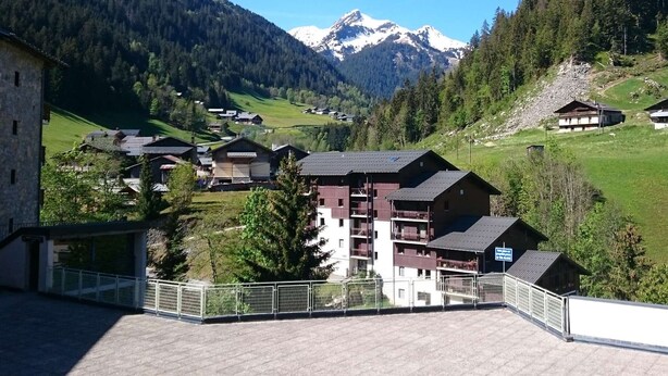 Ein Bergdorf mit traditionellen Holzhäusern, einem Steinhaus und Blick auf schneebedeckte Gipfel.