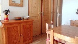 Ein Holzes Esstisch mit Stühlen, ein Holzschrank mit Küchenutensilien und zwei Holztüren.