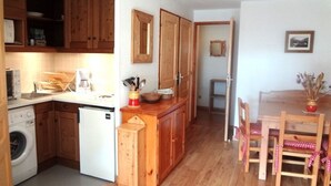 Eine kleine Küche mit Holzschränken, einer Waschmaschine und einem Essbereich mit Tisch und Stühlen.