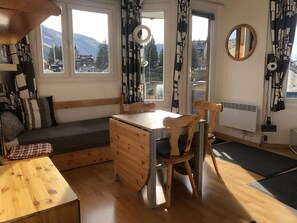 A cozy room with a wooden table, two chairs, a bench, and a window with a view of mountains. - Avoriaz: A magnificent apartment in the heart of the resort (Morzine)
