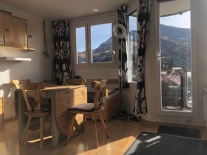 A cozy kitchen with wooden furniture, a dining table, and a view of mountains through large windows. - Avoriaz: A magnificent apartment in the heart of the resort (Morzine)