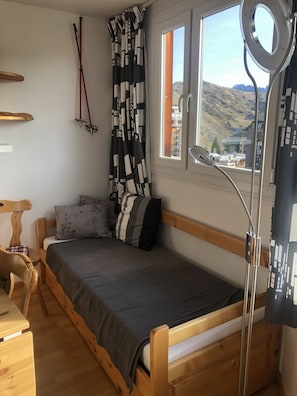 Um quarto pequeno e acolhedor com uma cama de madeira, uma janela com vista para montanhas e um telescópio no parapeito.