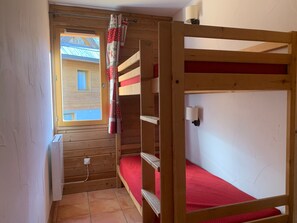 A small, wooden room with a bunk bed, a window with a view of a building, and a wall-mounted lamp. - Charming 2P with balcony and parking, Pra Loup (Pra-Loup)
