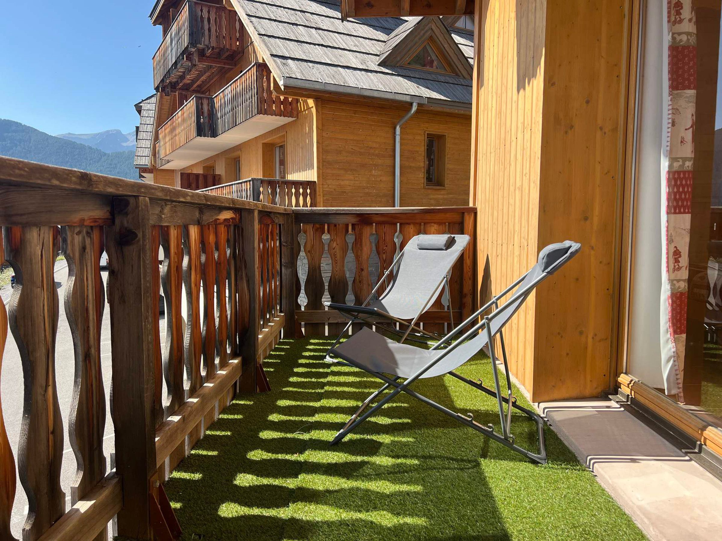 Un bâtiment en bois doté d’un balcon, de deux fauteuils inclinables et offrant une vue sur les montagnes.