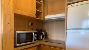 Eine kleine Küche mit Holzausstattung, einer Mikrowelle, einer Kaffeemaschine, einem Kühlschrank und einer Spüle aus Edelstahl.