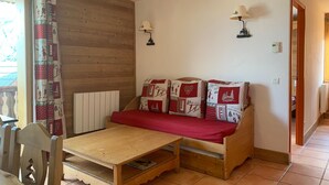 Ein gemütliches Zimmer mit Holzboden, einem Holztisch, einer Couch mit gemusterten Kissen und zwei Wandlampen.