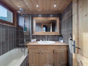 A modern bathroom with a wooden vanity, a large mirror, and a bathtub.
