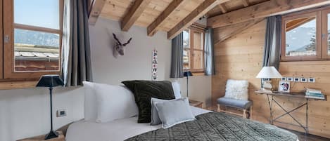 Un dormitorio acogedor con techo de madera, una cama con colcha verde, una cabeza de animal montada y un escritorio con lámpara y libros.